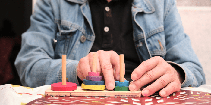 A patient performing a skill-strengthening exercise. The patient's face is not visible, and their hands are in the foreground.