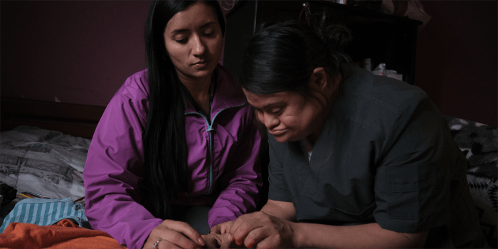 Two women sewing a blanket. The younger woman is helping the older with the task.