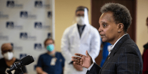 Chicago Mayor Lori Lightfoot speaks at a podium with medical personnel nearby.
