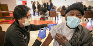 From left to right, a doctor is providing a patient with a dose of the COVID-19 vaccine