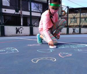 A masked child draws with sidewalk chalk in a schoolyard in Bogota, Colombia