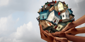 Several hands holding a cluster of various colored homes in a circular shape