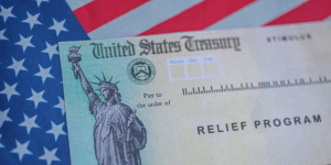 A photo of a United States Treasury "Relief Program" check resting on an American Flag.