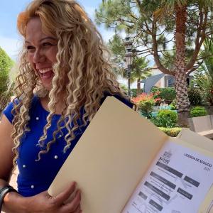 A happy, smiling woman holding her approved business license permit paperwork as part of the Visor Urbano program.
