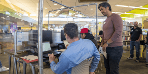 Two men apply for jobs on library-provided laptops while a volunteer answers questions.
