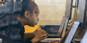 A woman leaning in close to a laptop screen as seen through a large window.
