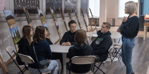 A teacher speaking to a group of students at a round table.
