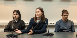 Three students sitting next to each other. The student in the middle is sharing their thoughts.