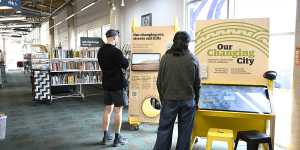 Two people standing in front of an exhibit, reads "our changing city"
