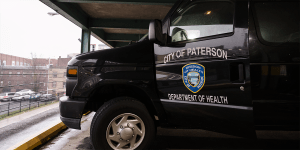 A black van parked inside a parking garage.  The front driver's side door is open and reads, "City of Paterson Department of Health."