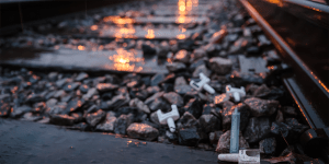 Railroad tracks that are slick with rain.  On the rocks between the ties lie discarded drug paraphernalia.  The tracks stretch into the distance.,