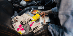 The front passenger seat of a car that is filled with loose, cluttered items.  Among them are boxes of Narcan, a scarf, and other miscellaneous items.