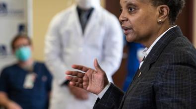 Chicago Mayor Lori Lightfoot speaks at a podium with medical personnel nearby.