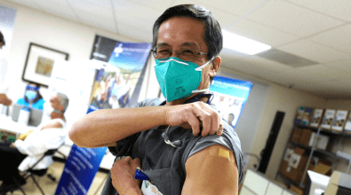 A doctor lifting up his left shoulder sleeve to show a bandage signaling that he has received a COVID-19 vaccine