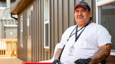 A portrait of a smiling resident sitting outside of his apartment in The Melody, a shipping container housing community in Atlanta.  The community was build and occupied as part of the Rapid Housing program.