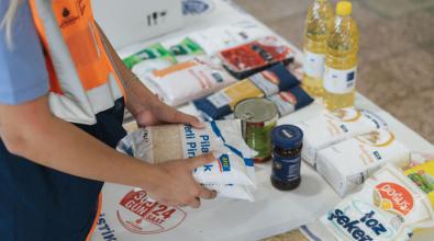 An up-close view of a woman's hands holding two bags of rice as a part of a table with an assortment of dry goods being packaged for residents in the Pay It Forward program.
