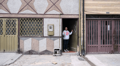 A woman stands in an open doorway of a building in a worn block of businesses.