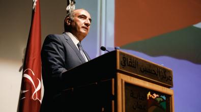 A photo of a speaker behind a podium announcing the launch of the Amman is Listening program.