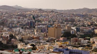 View of downtown Abha, Saudi Arabia, with colorful buildings in the foreground and mountains in the background.
