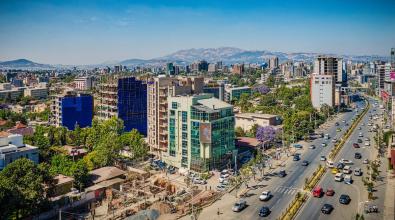 Panoramic view of Addis Ababa, Ethiopia, showing city buildings and busy street in the foreground, stretching toward mountains in the background.