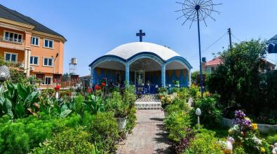 Holy Cross Cathedral in Benin City, Nigeria, lit by bright sunlight and surrounded by green plants and colorful flowers.
