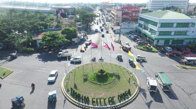 A roundabout in Naga City, Philippines, with a grassy knoll at its center. Letters on the grass read, "Pilgrim City of Naga."
